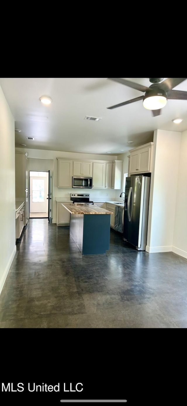 kitchen with a kitchen island, finished concrete flooring, appliances with stainless steel finishes, light countertops, and baseboards