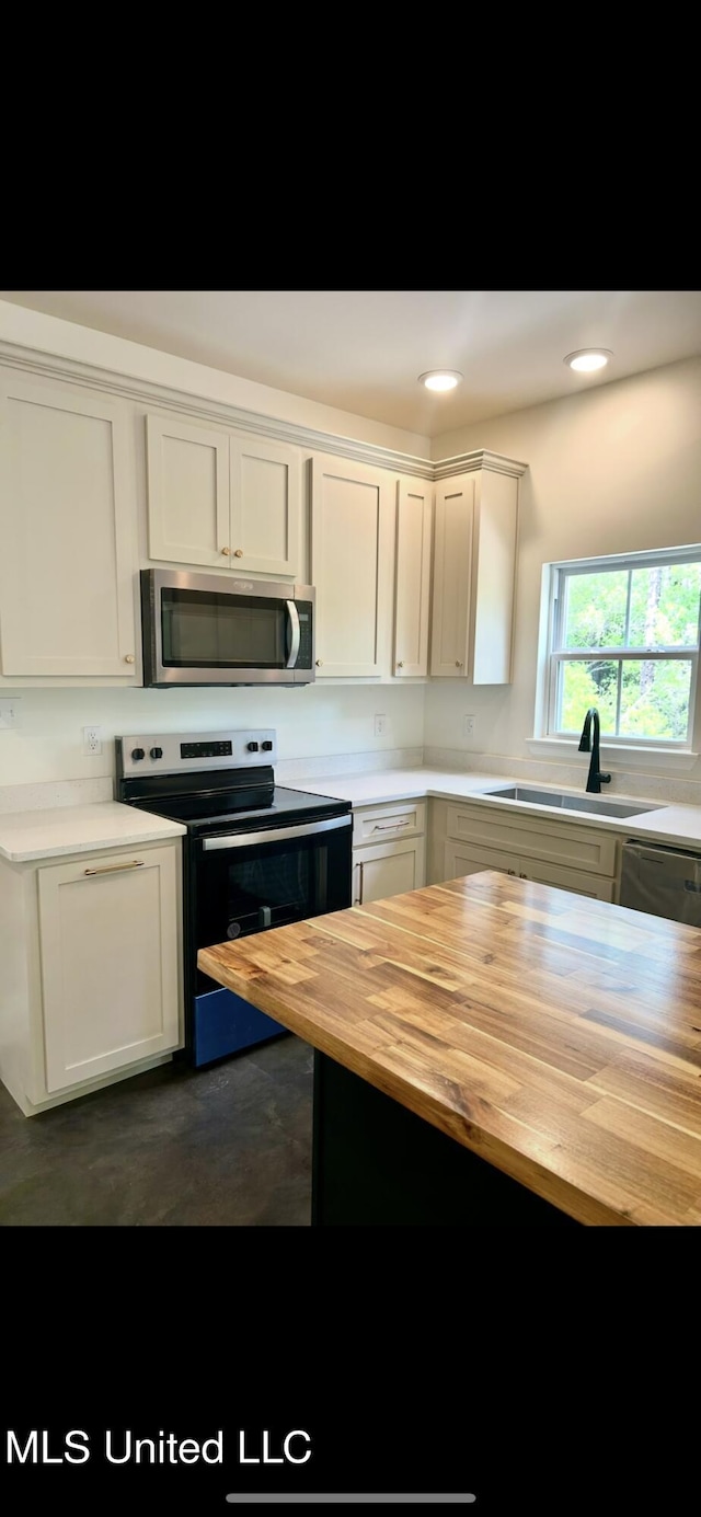kitchen with a sink, concrete floors, stainless steel appliances, white cabinetry, and butcher block counters