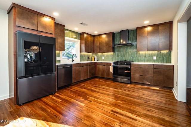 kitchen featuring tasteful backsplash, dark brown cabinetry, stainless steel appliances, dark wood-type flooring, and wall chimney range hood