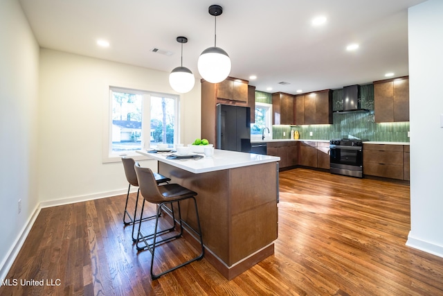 kitchen featuring wall chimney exhaust hood, dark hardwood / wood-style flooring, decorative light fixtures, a kitchen island, and black appliances