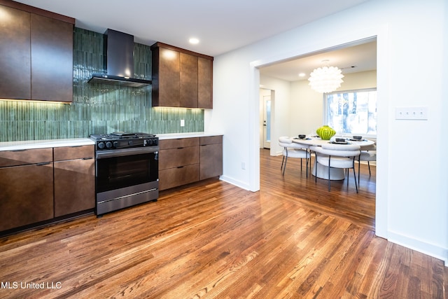 kitchen with wall chimney exhaust hood, stainless steel gas stove, dark brown cabinets, and wood-type flooring