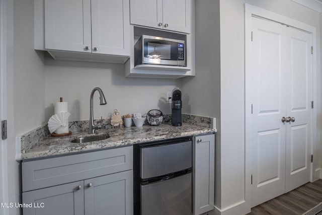 kitchen featuring light stone counters, appliances with stainless steel finishes, hardwood / wood-style flooring, gray cabinetry, and sink