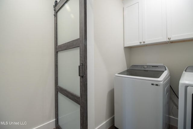 clothes washing area with a barn door, washing machine and dryer, and cabinets