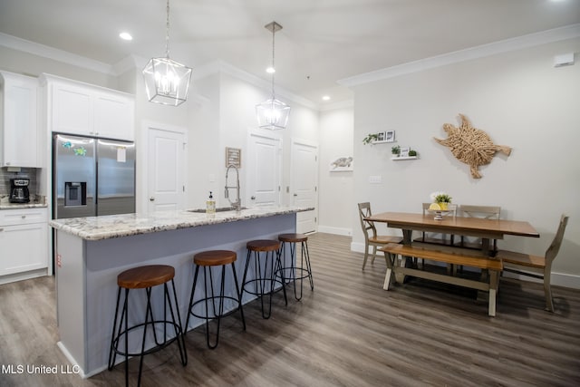 kitchen with white cabinets, a center island with sink, hanging light fixtures, stainless steel refrigerator with ice dispenser, and sink