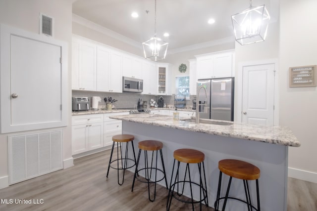 kitchen with decorative backsplash, an island with sink, crown molding, white cabinetry, and appliances with stainless steel finishes