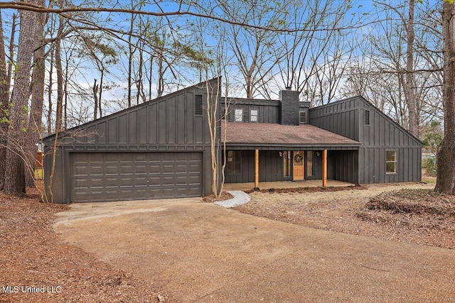 mid-century modern home with a chimney, covered porch, board and batten siding, a garage, and driveway