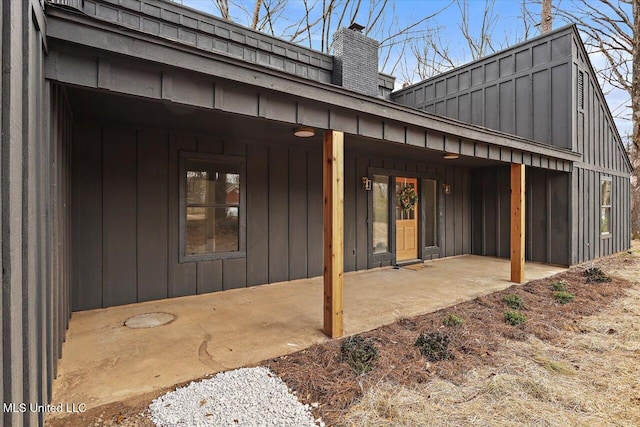 rear view of property with a chimney, board and batten siding, and a patio