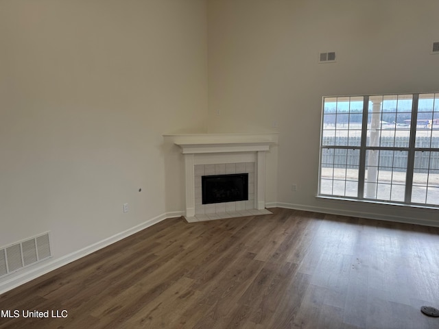 unfurnished living room with a tile fireplace, dark hardwood / wood-style floors, and a towering ceiling