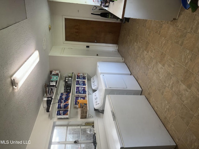 clothes washing area featuring a textured wall, washer and clothes dryer, and laundry area