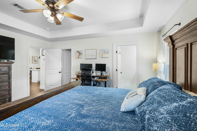 bedroom featuring a tray ceiling, wood finished floors, visible vents, and baseboards