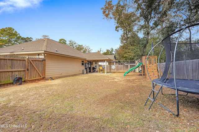 view of yard featuring a trampoline, a playground, and a fenced backyard