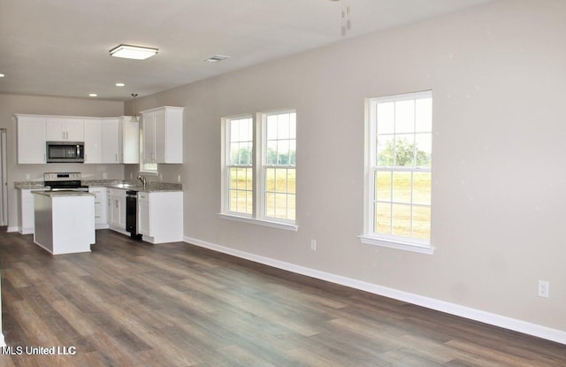 kitchen featuring white cabinets, a center island, dark hardwood / wood-style flooring, stainless steel appliances, and light stone counters