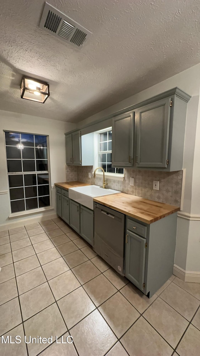 kitchen featuring sink, wooden counters, light tile patterned floors, dishwasher, and decorative backsplash