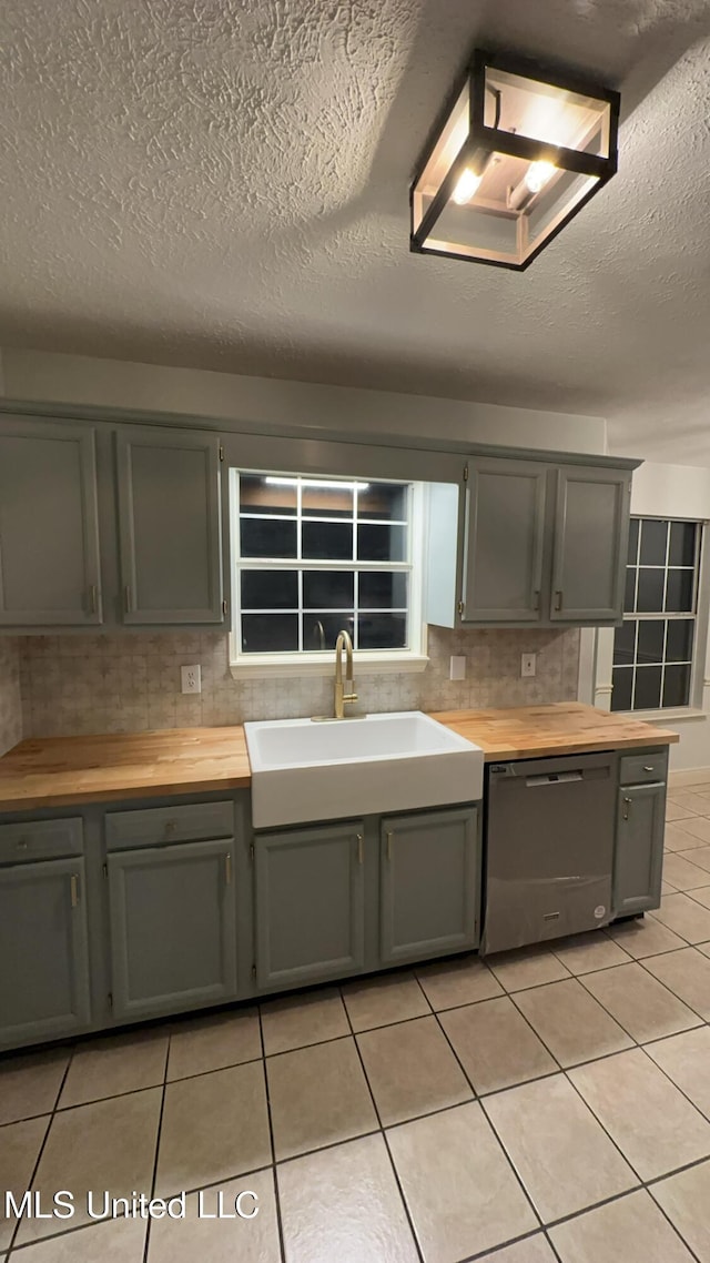 kitchen featuring sink, light tile patterned floors, dishwasher, a textured ceiling, and decorative backsplash