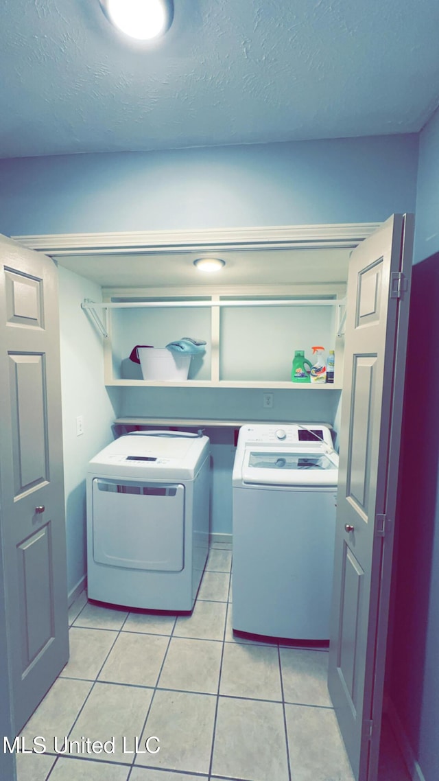 clothes washing area featuring washing machine and dryer, light tile patterned floors, and a textured ceiling