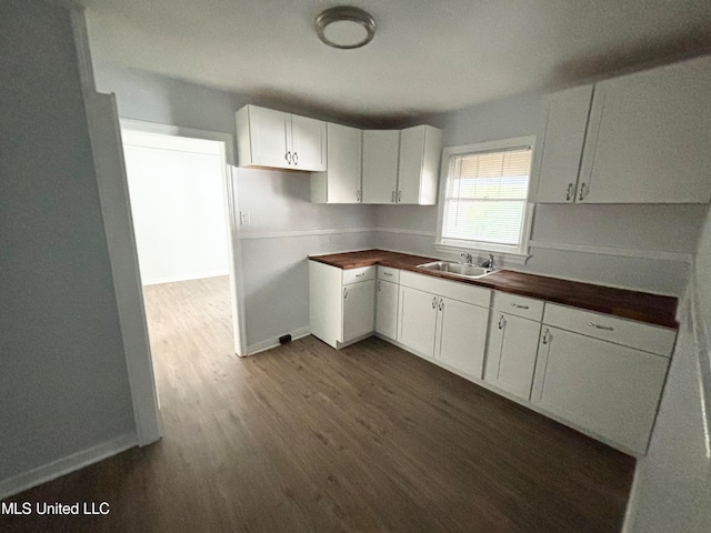 kitchen with wooden counters, sink, white cabinets, and dark wood-type flooring