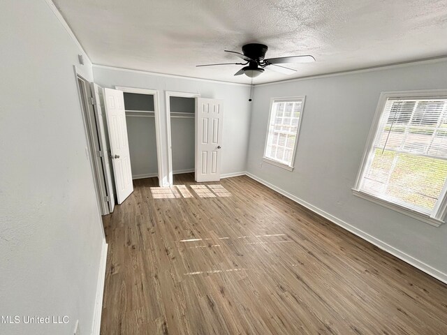 unfurnished bedroom featuring ceiling fan, a textured ceiling, multiple closets, hardwood / wood-style flooring, and crown molding