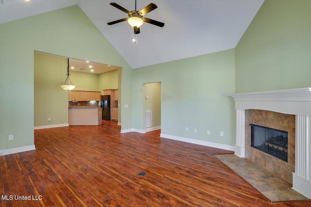 unfurnished living room featuring a tiled fireplace, high vaulted ceiling, ceiling fan, and dark hardwood / wood-style flooring