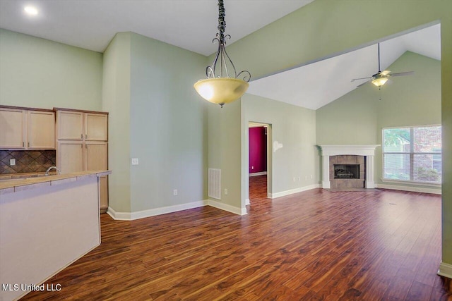 unfurnished living room featuring dark wood-type flooring, ceiling fan, high vaulted ceiling, and a tile fireplace