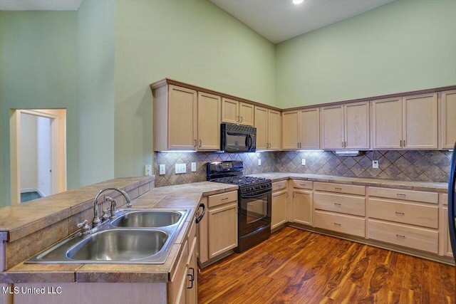 kitchen with dark wood-type flooring, kitchen peninsula, sink, black appliances, and a towering ceiling