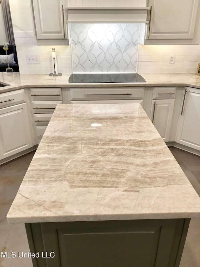 kitchen with backsplash, a center island, light stone counters, and black electric stovetop