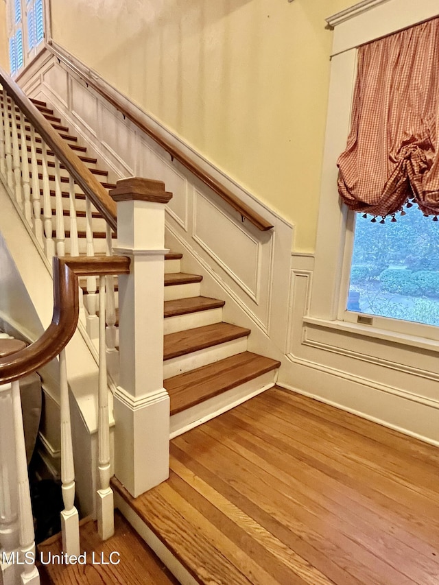 1211 River Rd, Greenwood, MS 38930 - staircase with a decorative wall, wood finished floors, a wainscoted wall, and plenty of natural light