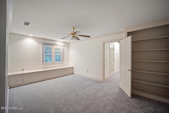 spare room featuring built in desk, crown molding, carpet flooring, a textured ceiling, and ceiling fan