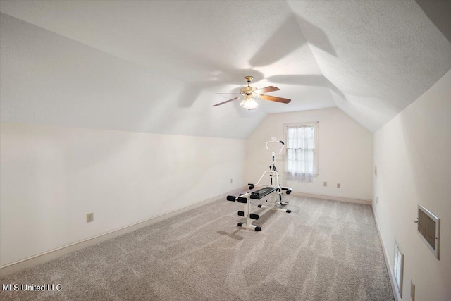 exercise room with a textured ceiling, ceiling fan, light colored carpet, and vaulted ceiling