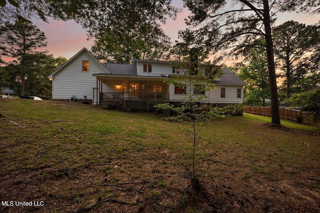 back house at dusk featuring a yard and covered porch