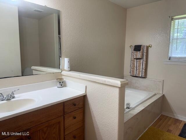 full bathroom with a bath, vanity, and wood finished floors