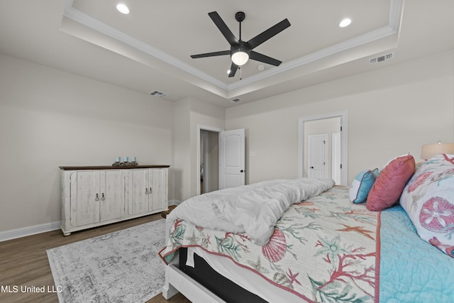 bedroom with a raised ceiling, visible vents, and wood finished floors