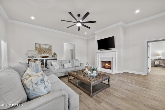 living room with light wood-style floors, ornamental molding, ceiling fan, a lit fireplace, and baseboards