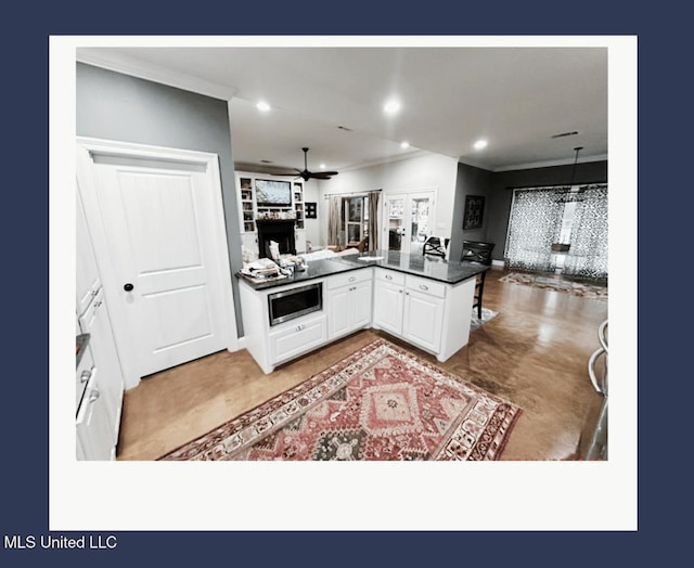 kitchen featuring stainless steel microwave, decorative light fixtures, white cabinetry, ceiling fan, and kitchen peninsula