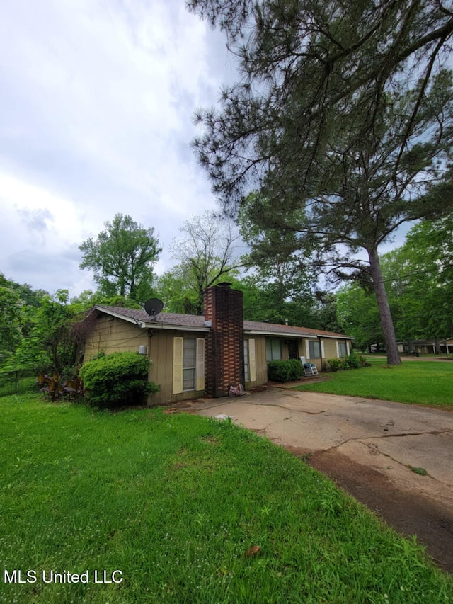 view of front facade featuring a chimney, a front yard, and concrete driveway