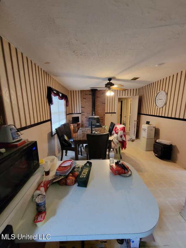 dining space featuring a wood stove, wallpapered walls, ceiling fan, a textured ceiling, and baseboards