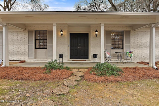 view of exterior entry with a porch and brick siding