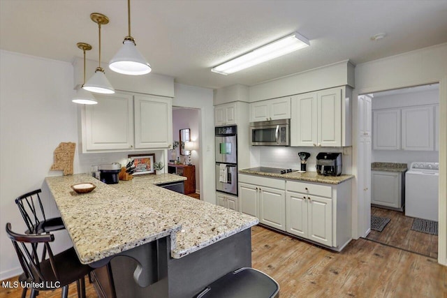 kitchen featuring washer / dryer, white cabinets, a breakfast bar area, a peninsula, and stainless steel appliances