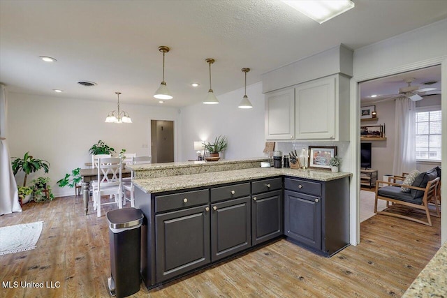 kitchen with light stone counters, a peninsula, visible vents, white cabinets, and light wood-type flooring