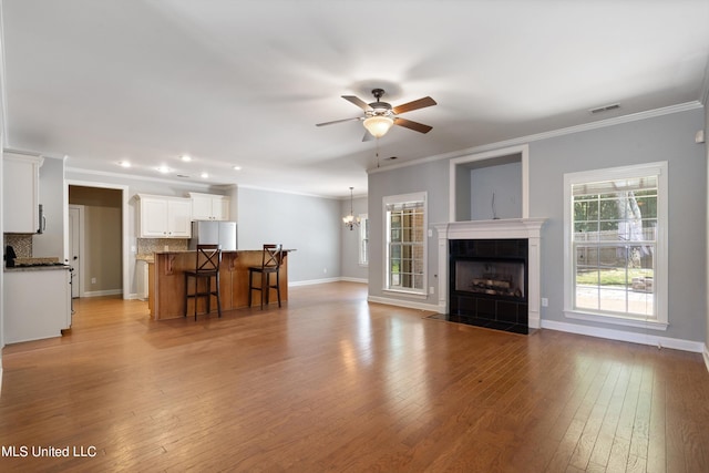 unfurnished living room featuring a tiled fireplace, ceiling fan with notable chandelier, light hardwood / wood-style flooring, and crown molding