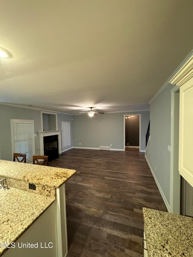 kitchen with dark wood-type flooring, light stone countertops, ceiling fan, and crown molding