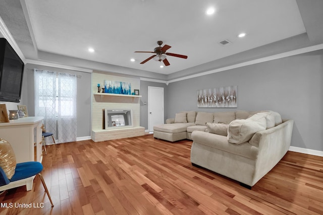 living room featuring ceiling fan, a fireplace, and light hardwood / wood-style flooring