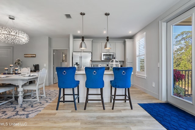 kitchen featuring visible vents, a center island with sink, a kitchen bar, light wood-style flooring, and stainless steel appliances