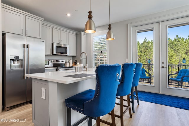 kitchen featuring light wood-type flooring, a kitchen bar, decorative light fixtures, french doors, and appliances with stainless steel finishes