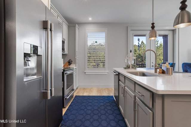 kitchen with gray cabinetry, stainless steel appliances, light countertops, and a sink