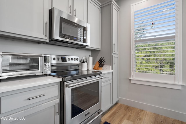 kitchen featuring baseboards, light wood finished floors, a toaster, stainless steel appliances, and light countertops