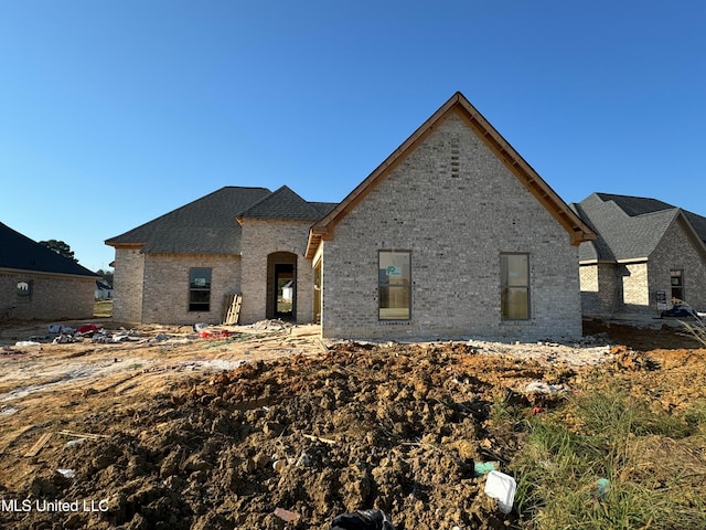 french country style house with roof with shingles and brick siding