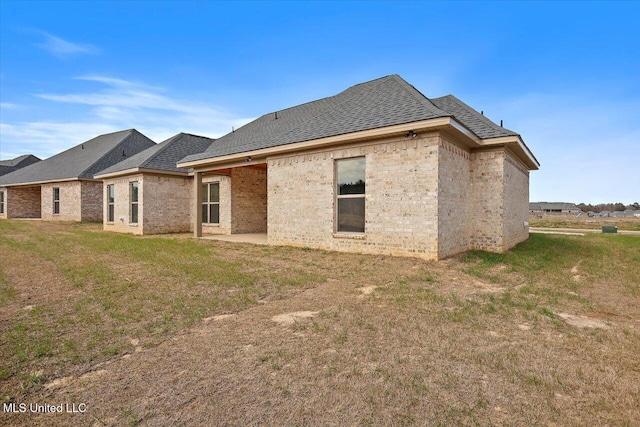 rear view of house featuring a yard, brick siding, a patio, and roof with shingles