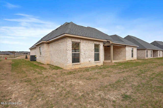 back of house with a yard, a shingled roof, cooling unit, and brick siding