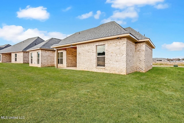 back of property with brick siding, roof with shingles, and a yard