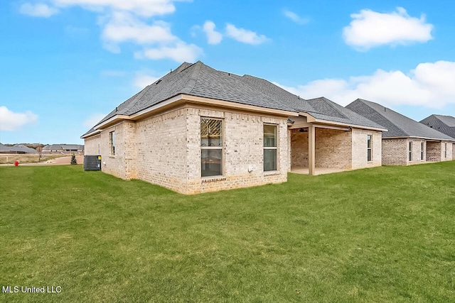 rear view of house with roof with shingles, central AC unit, a lawn, and brick siding